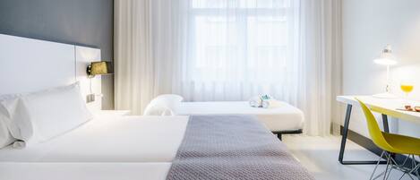 A hotel room with two beds, a desk, a chair, and a window with curtains.