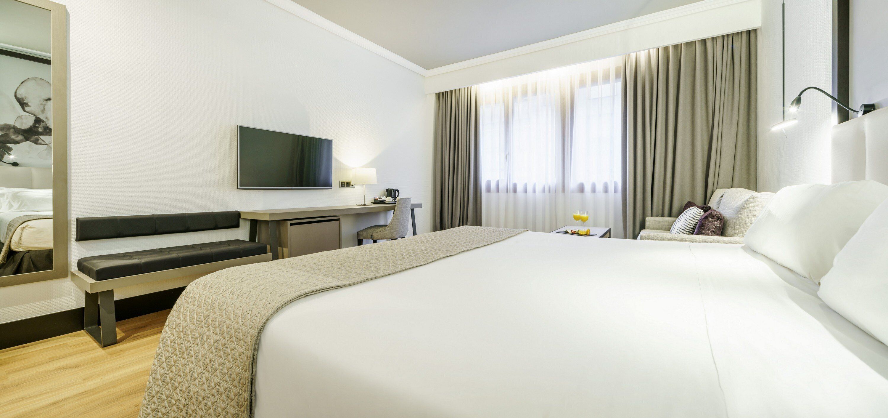 Habitación de hotel con una cama grande, un escritorio con silla, televisor y ventana con cortinas.