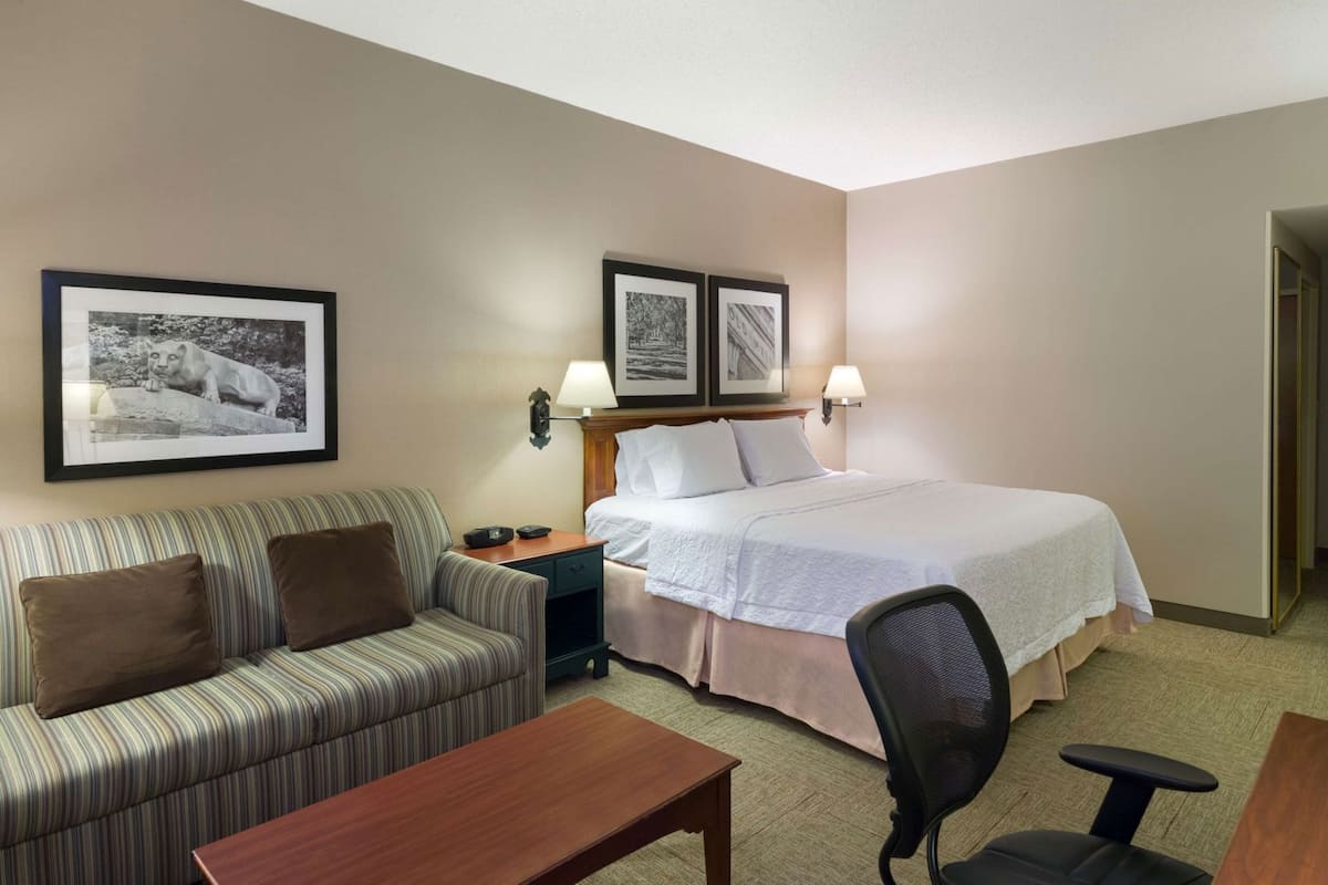 A hotel room with a bed, a sofa, a desk, and two wall-mounted lamps.