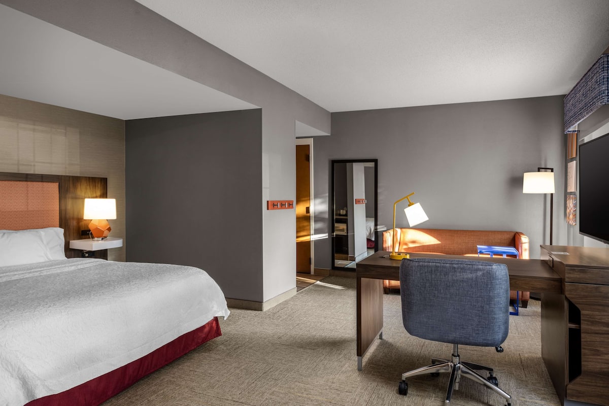 A hotel room with a large bed, a desk with a chair, a TV, and a lamp.