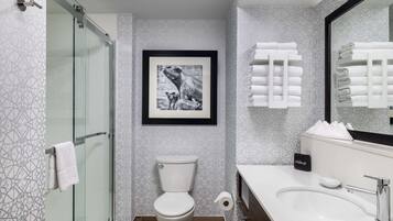 Un baño moderno con ducha de vidrio, inodoro, lavamanos y un cuadro enmarcado en la pared.