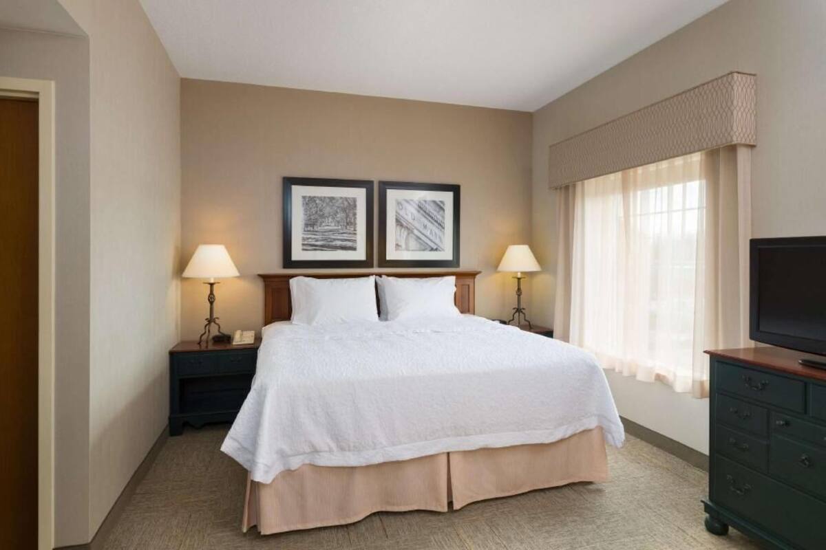 A hotel room with a bed, two bedside lamps, a television, and two framed pictures on the wall.