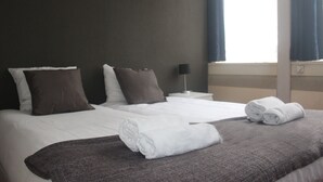 Een hotelkamer met twee bedden, donkere wanden en een raam met gordijnen.