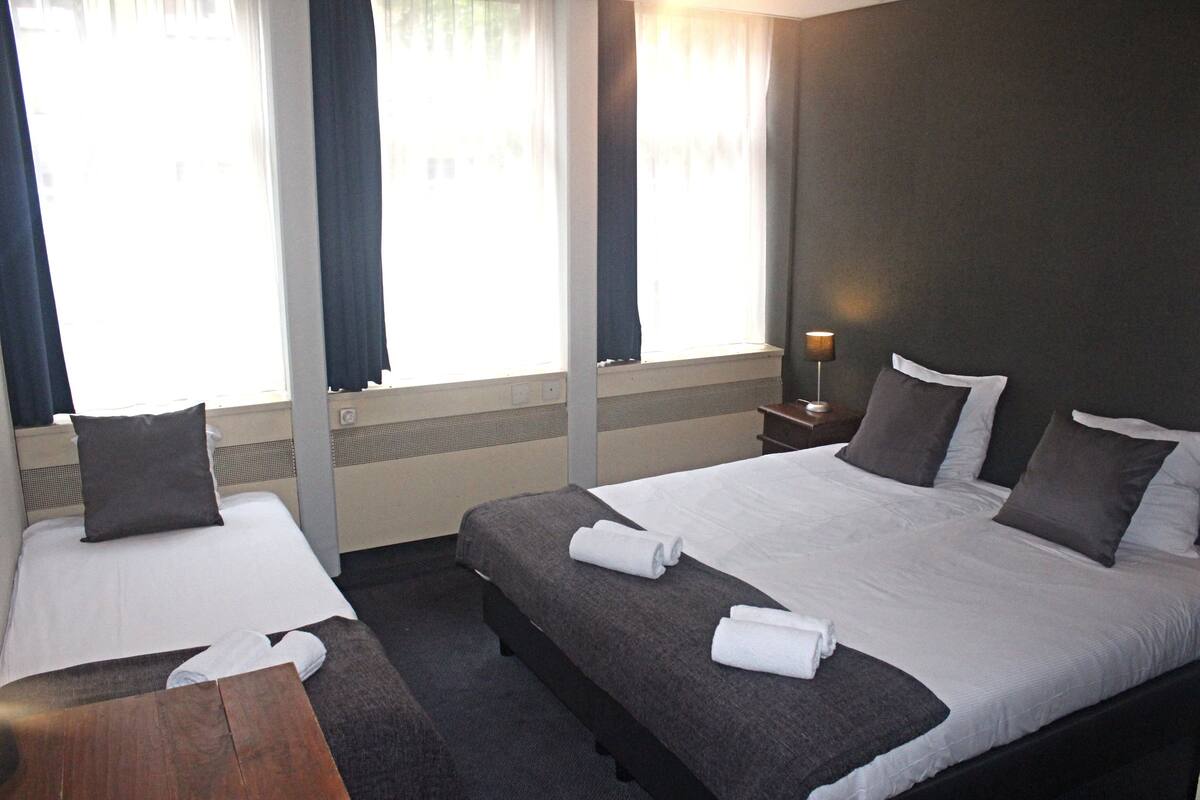A hotel room with two single beds, a small wooden table, and a nightstand with a lamp.