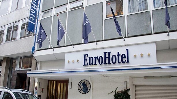 Het uiterlijk van EuroHotel met een bord, een geparkeerde auto en een kleine plant bij de ingang.
