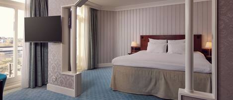 Habitación de hotel con una cama grande, un televisor montado en la pared y vistas de la ciudad desde la ventana.