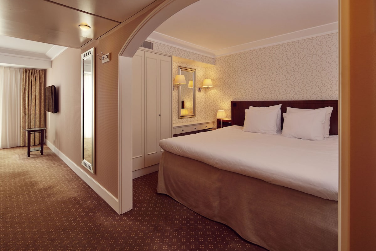 A hotel room with a large bed, a mirror, a dresser, and a television.