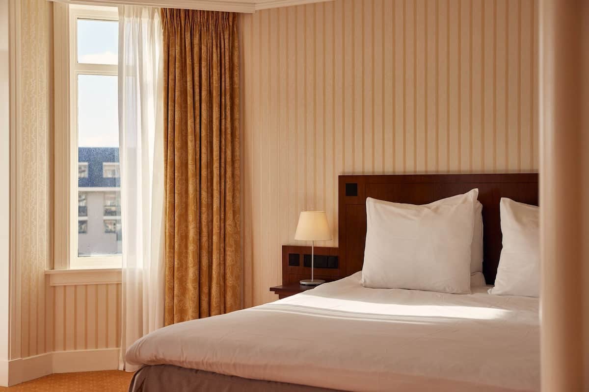 A hotel room with a large bed, a nightstand with a lamp, and a window with curtains.
