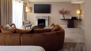 Ein modernes Hotelzimmer mit einem großen braunen Sofa, einem flachbildfernseher an der Wand, einem Kamin und einem Beistelltisch mit Dekorationen.