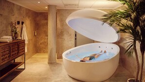 A large, round hot tub with a person relaxing inside, a wooden cabinet with towels, and a potted plant.