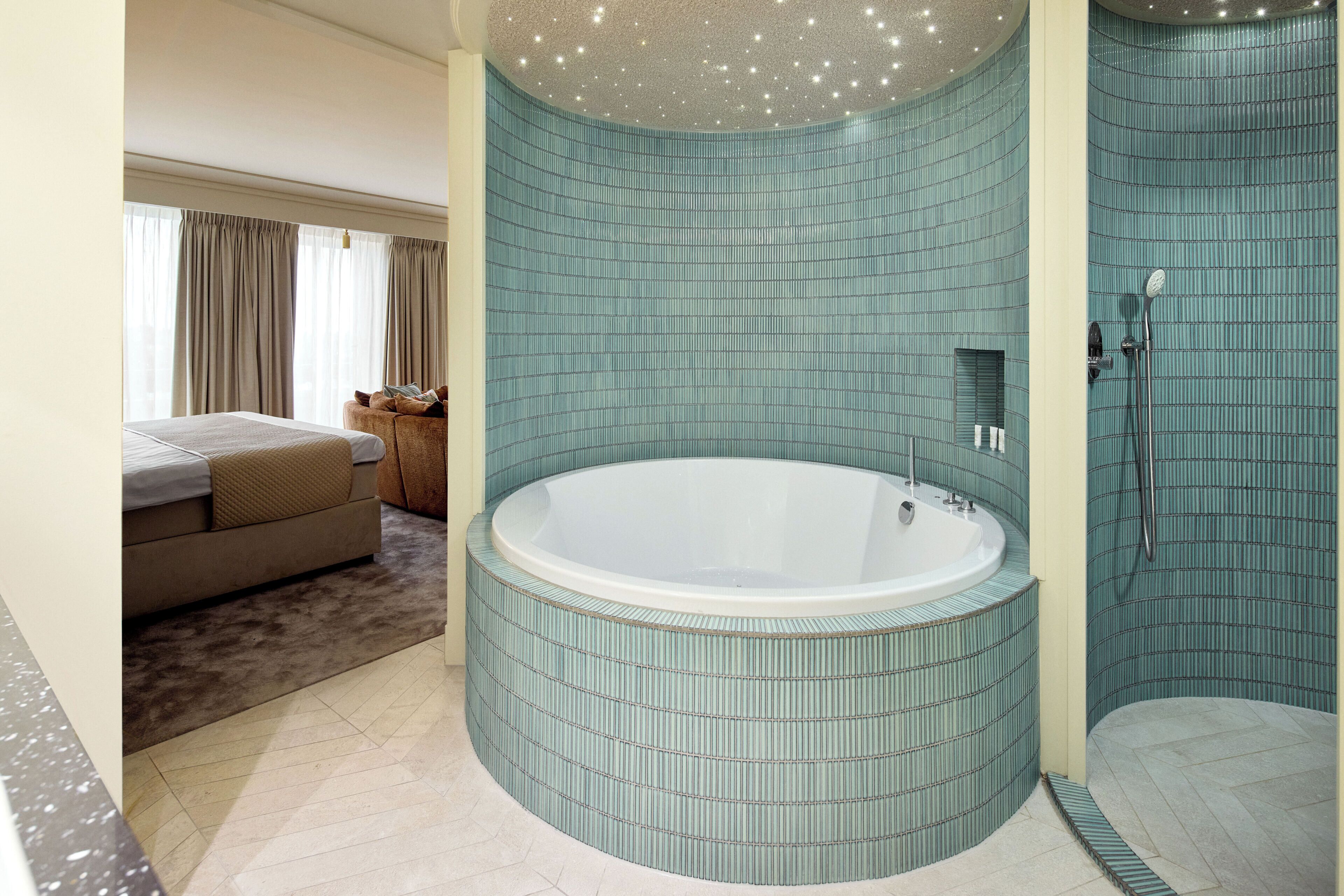 Une salle de bain avec une grande baignoire, un espace douche et une chambre séparée avec un lit et des rideaux.