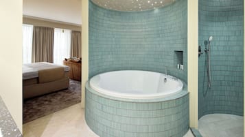 A bathroom with a large bathtub, a shower area, and a separate bedroom with a bed and curtains.