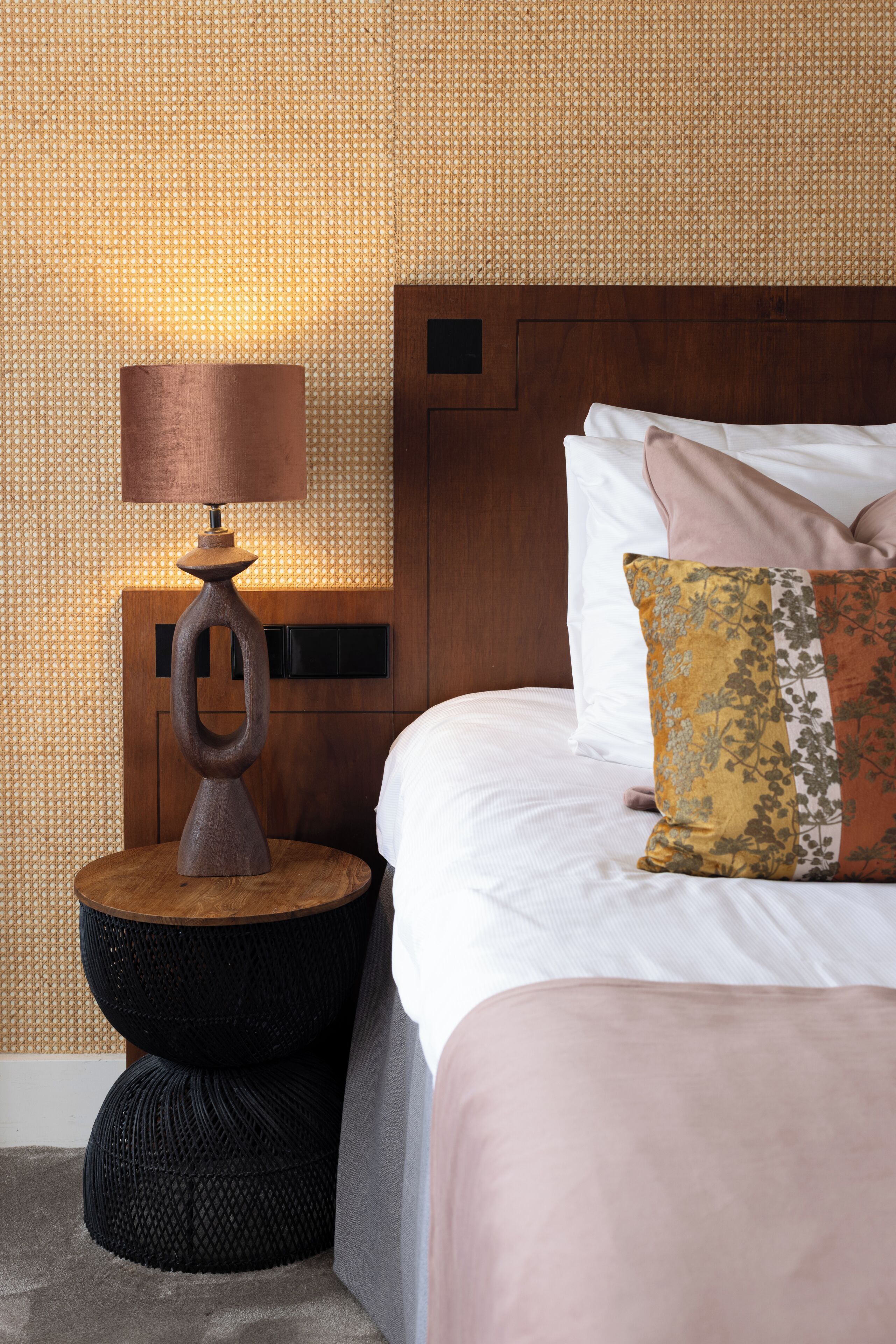 A hotel room with a bed, a nightstand with a lamp, and a textured wall.