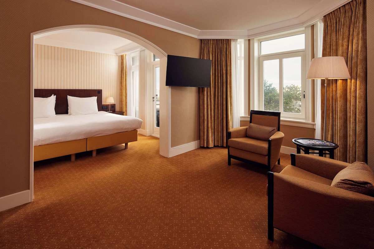 A hotel room with a large bed, a flat-screen TV, a sofa, and a small table.