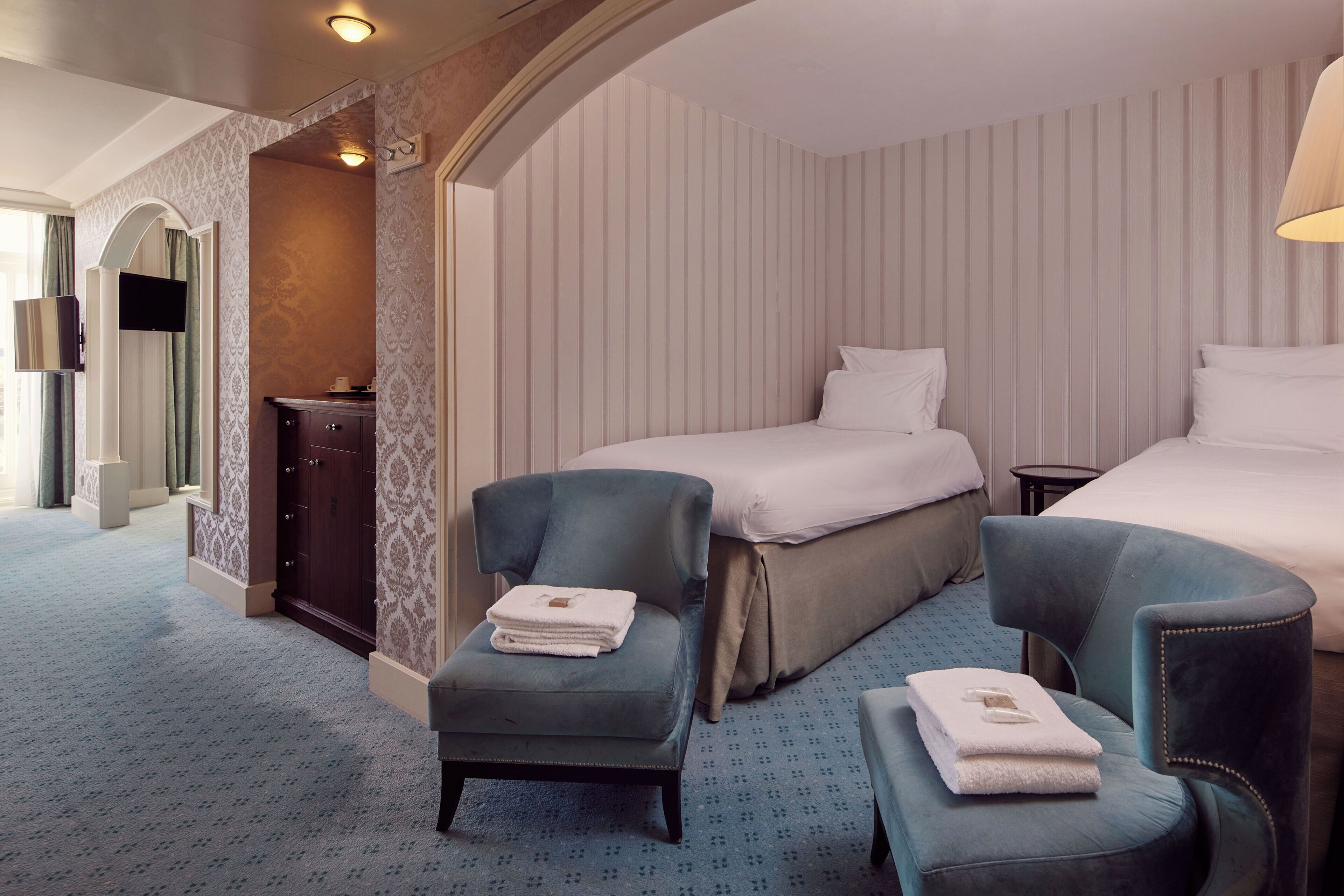 A hotel room with a bed, two armchairs, a small table, and a TV.