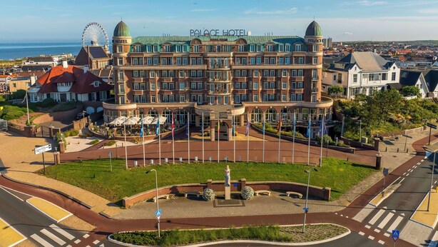 A large hotel with a prominent Ferris wheel in the background, a central courtyard, and a view of the sea.