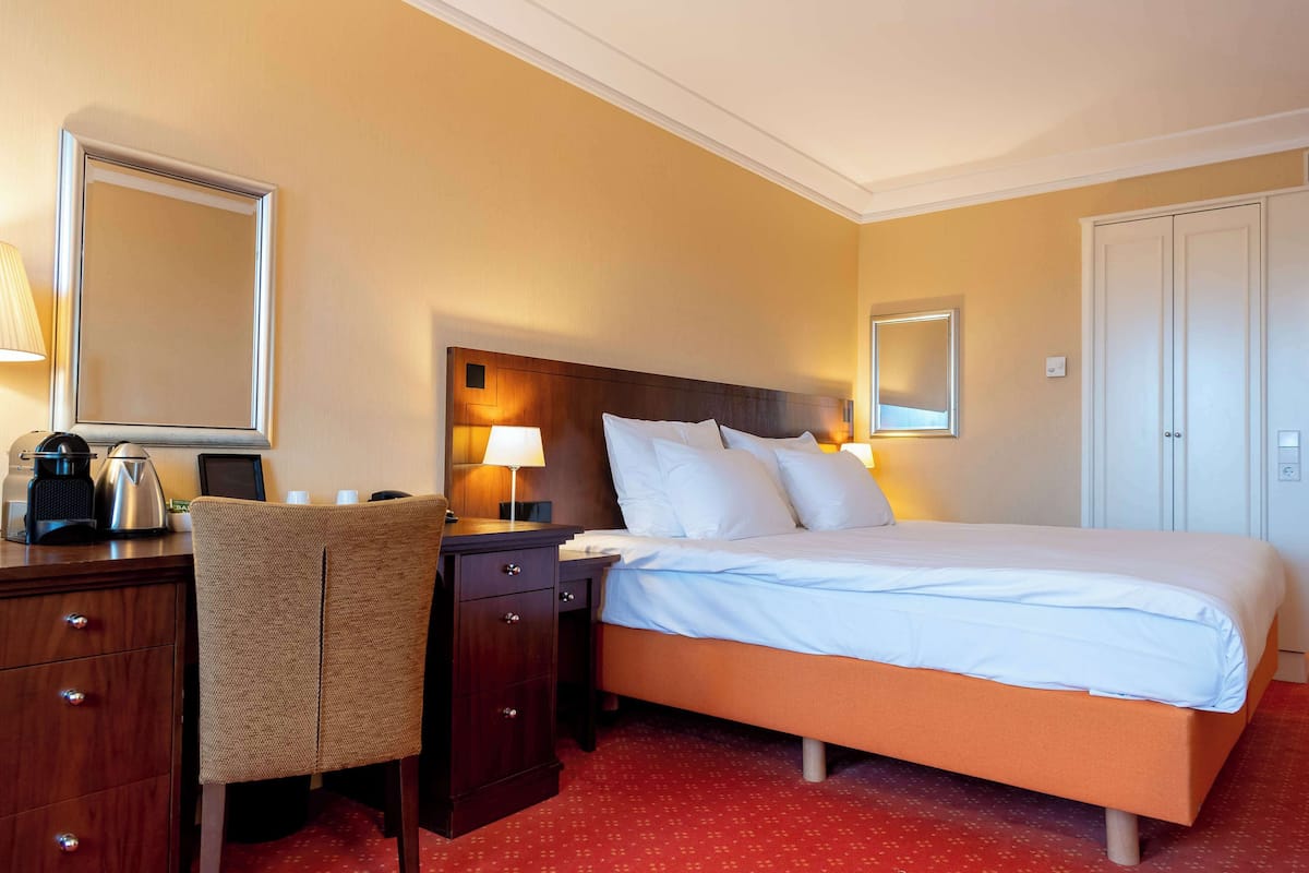 A hotel room with a bed, a desk with a chair, a lamp, and a mirror.