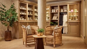 A room with wicker chairs, a round table, and a large potted plant. There are shelves with various items and a clothing rack in the background. - Van der Valk Palace Hotel Noordwijk (Noordwijk)