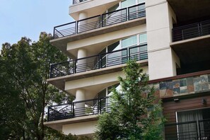 Edifici d'àmbit elevat amb balcons, grans finestres i façana combinada de formigó i pedra.