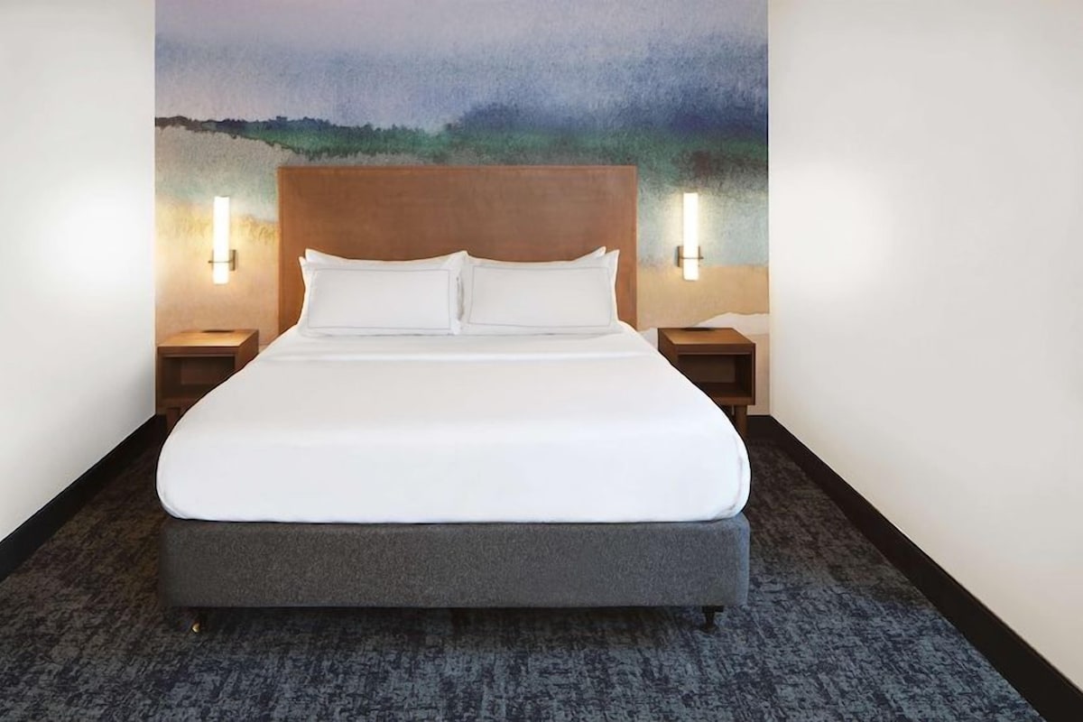 A hotel room with a large bed, two bedside tables with lamps, and a painting on the wall.