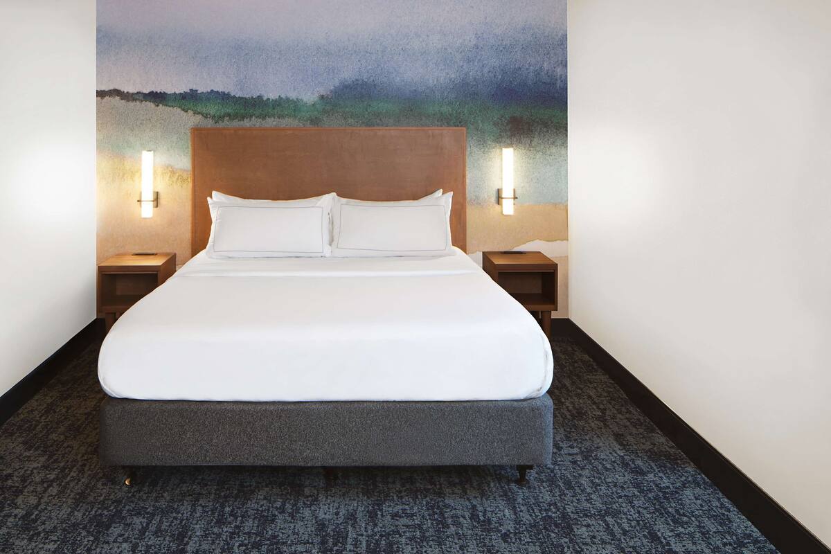 A hotel room with a large bed, two bedside tables with lamps, and a painting on the wall.