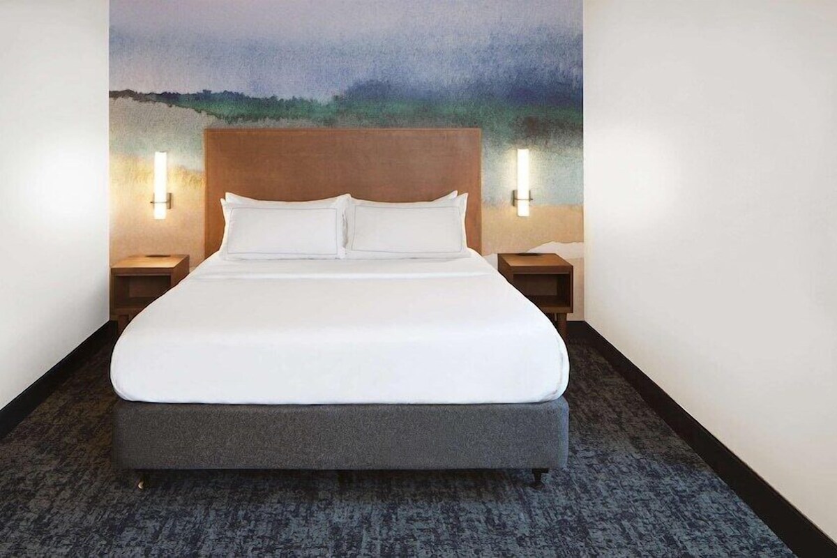 A hotel room with a large bed, two bedside tables with lamps, and a painting on the wall.