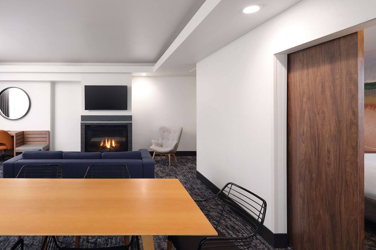 A hotel room with a wooden dining table, a sofa, a chair, a fireplace, and a bed with a headboard.
