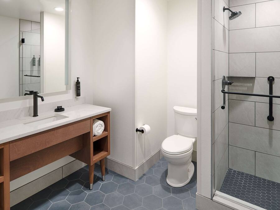Un baño moderno con un espejo grande, un lavabo, un inodoro y una zona de ducha.