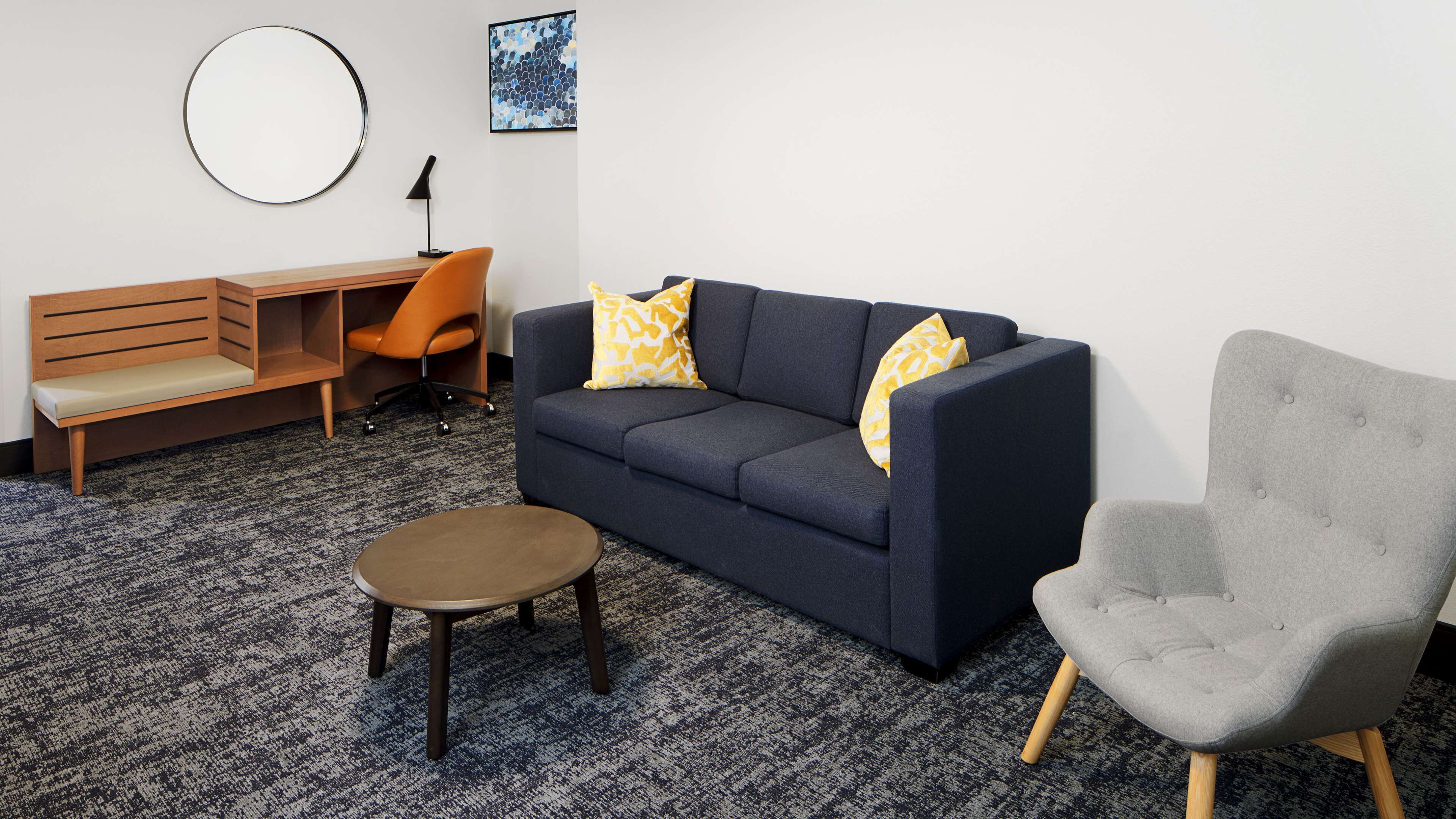 A modern living room with a dark blue sofa, a grey armchair, a wooden bench, and a small round table.