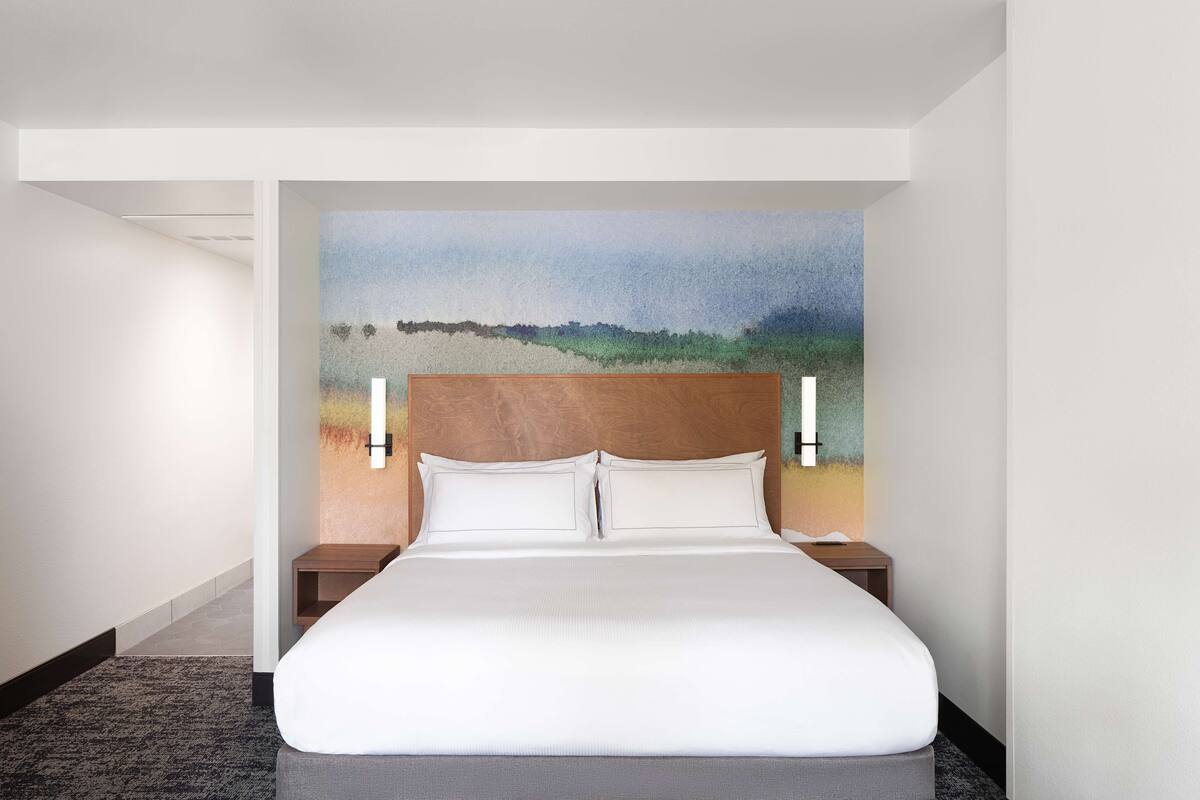 A hotel room with a large bed, a headboard with a painting, and two bedside tables.