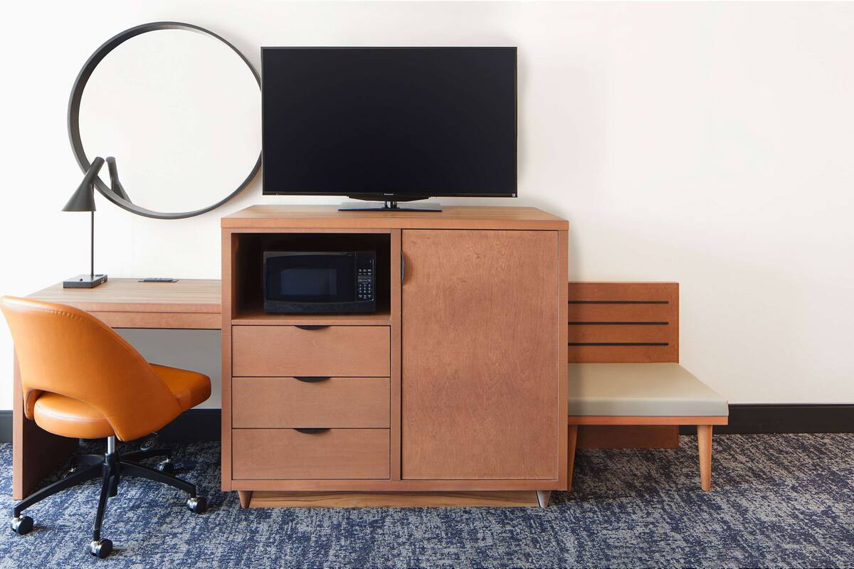 A compact workspace with a desk, a chair, a television, a microwave, and a ring light.