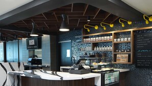A modern coffee shop interior with a curved counter, a menu board, and a display case with coffee items. - River's Edge Hotel Portland, Tapestry Collection by Hilton (Portland)