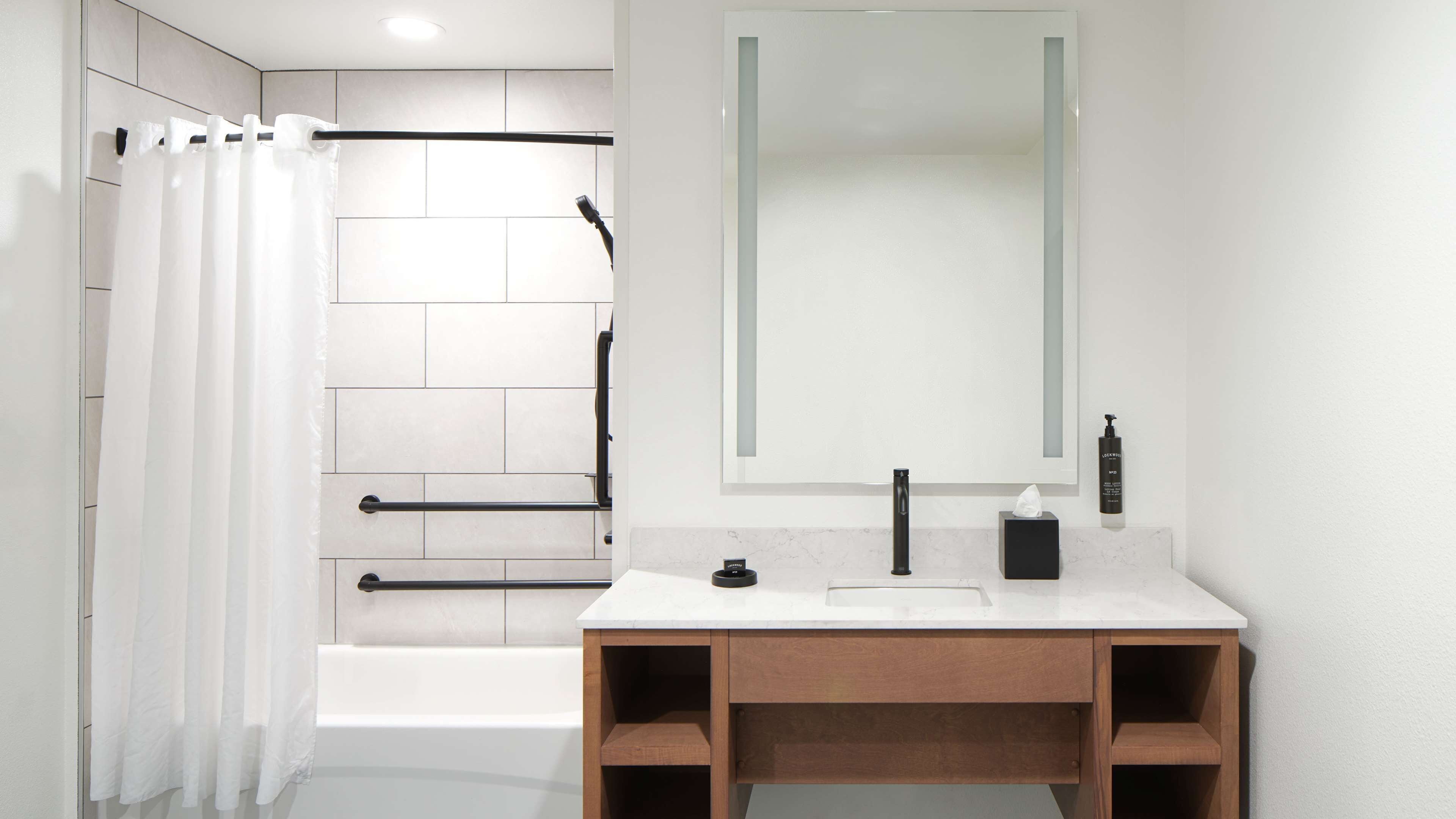 A modern bathroom with a bathtub, a shower curtain, a sink with a mirror, and toiletries.