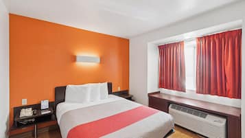 Habitación de hotel con cama, mesita de noche con teléfono, lámpara de pared, ventana con cortinas y un calentador.