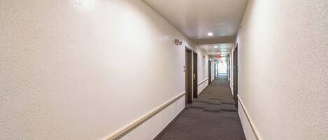 A long, narrow hotel corridor with carpeted floors and white walls.