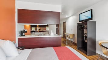 A hotel room with a bed, a desk, a television, and a kitchenette.