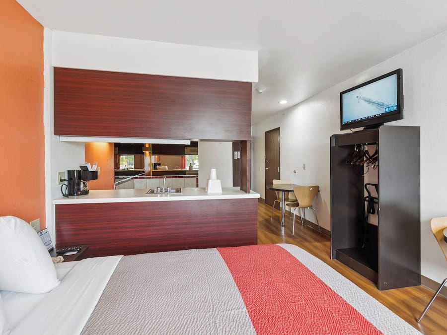 A hotel room with a bed, a desk, a television, and a kitchenette.