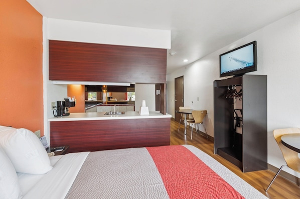 A hotel room with a bed, a desk, a television, and a kitchenette.