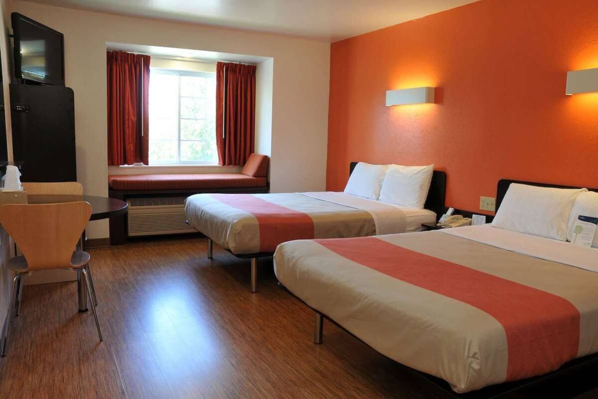 Habitación de hotel con dos camas, un escritorio, una silla, un televisor y una ventana con cortinas.
