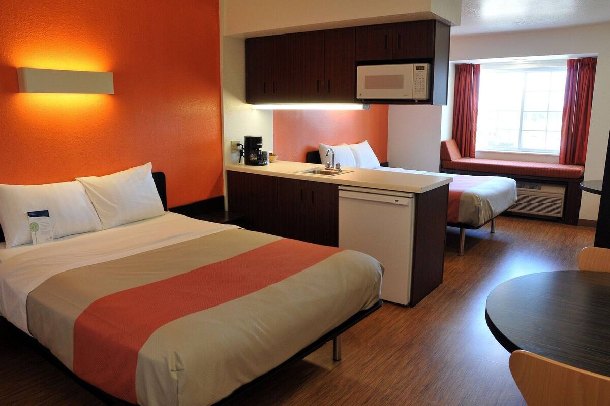 Habitación de hotel con cama, una kitchenette pequeña, microondas, cafetera y ventana con cortinas.