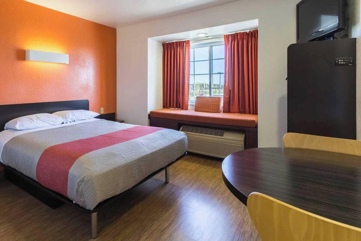 Una habitación de hotel con cama, ventana con cortinas, escritorio y televisor.