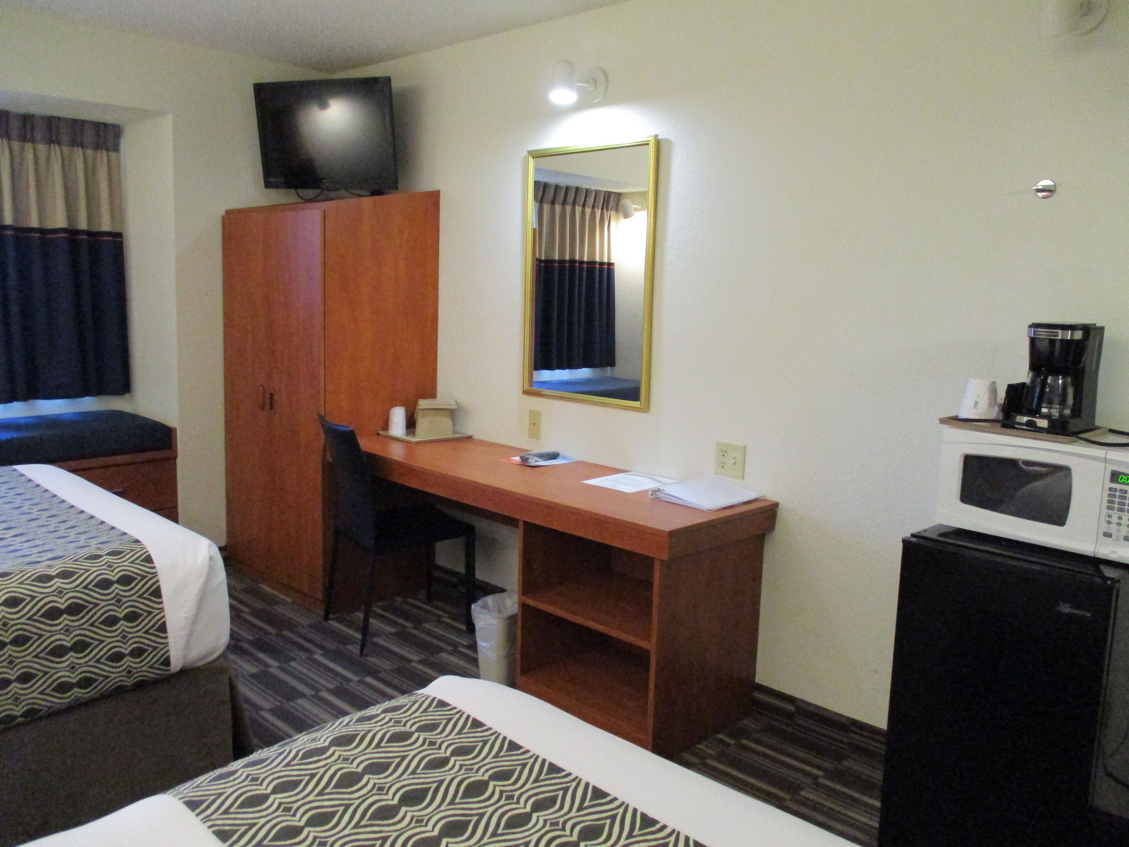 A hotel room with two beds, a desk, a chair, a television, a mirror, a coffee maker, and a microwave.