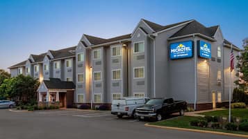 Een Microtel hotel met een gevel van baksteen, meerdere kamers en een parkeerplaats met voertuigen.