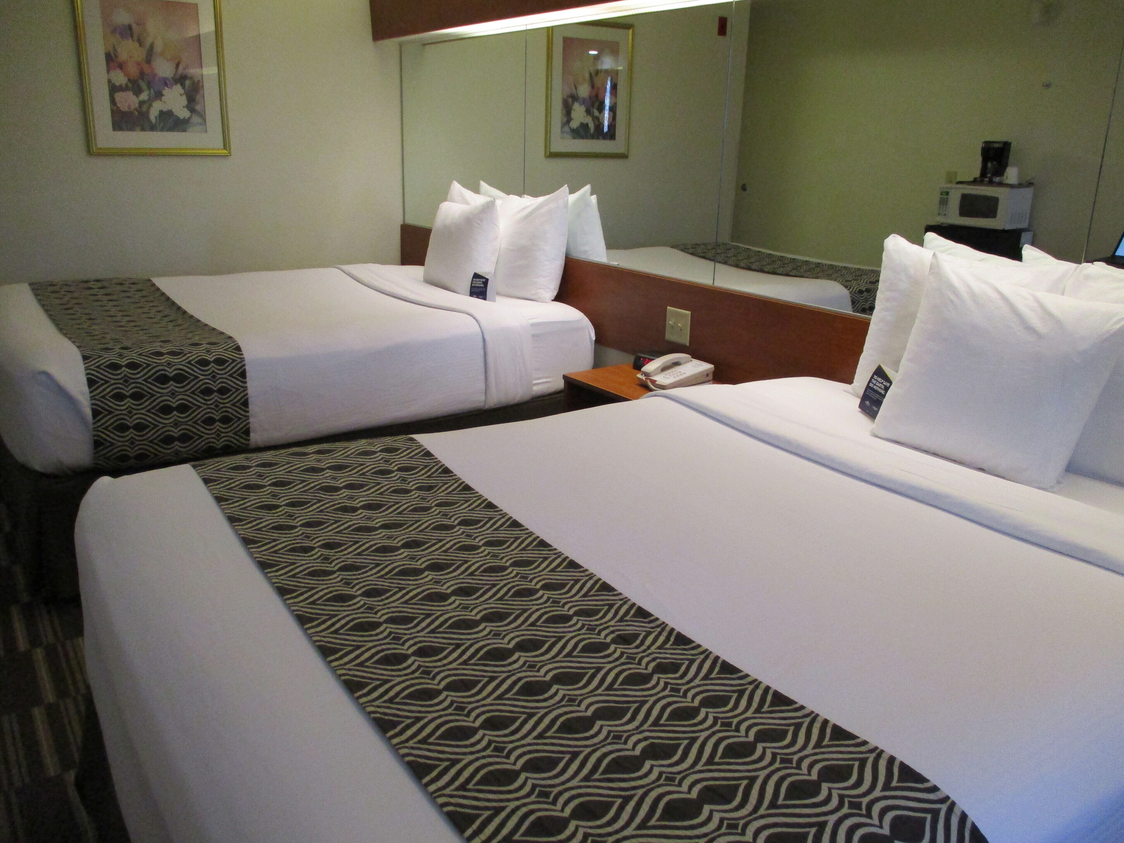 Habitación de hotel con dos camas, una mesita de noche con teléfono y un microondas sobre una pequeña mesa.