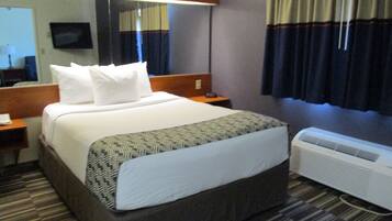 Habitación de hotel con una cama grande, una mesita de noche con lámpara, un televisor de pantalla plana en la pared y una ventana con cortinas.