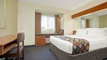 Una habitación de hotel con cama, escritorio, silla, ventana con cortinas y espejo.