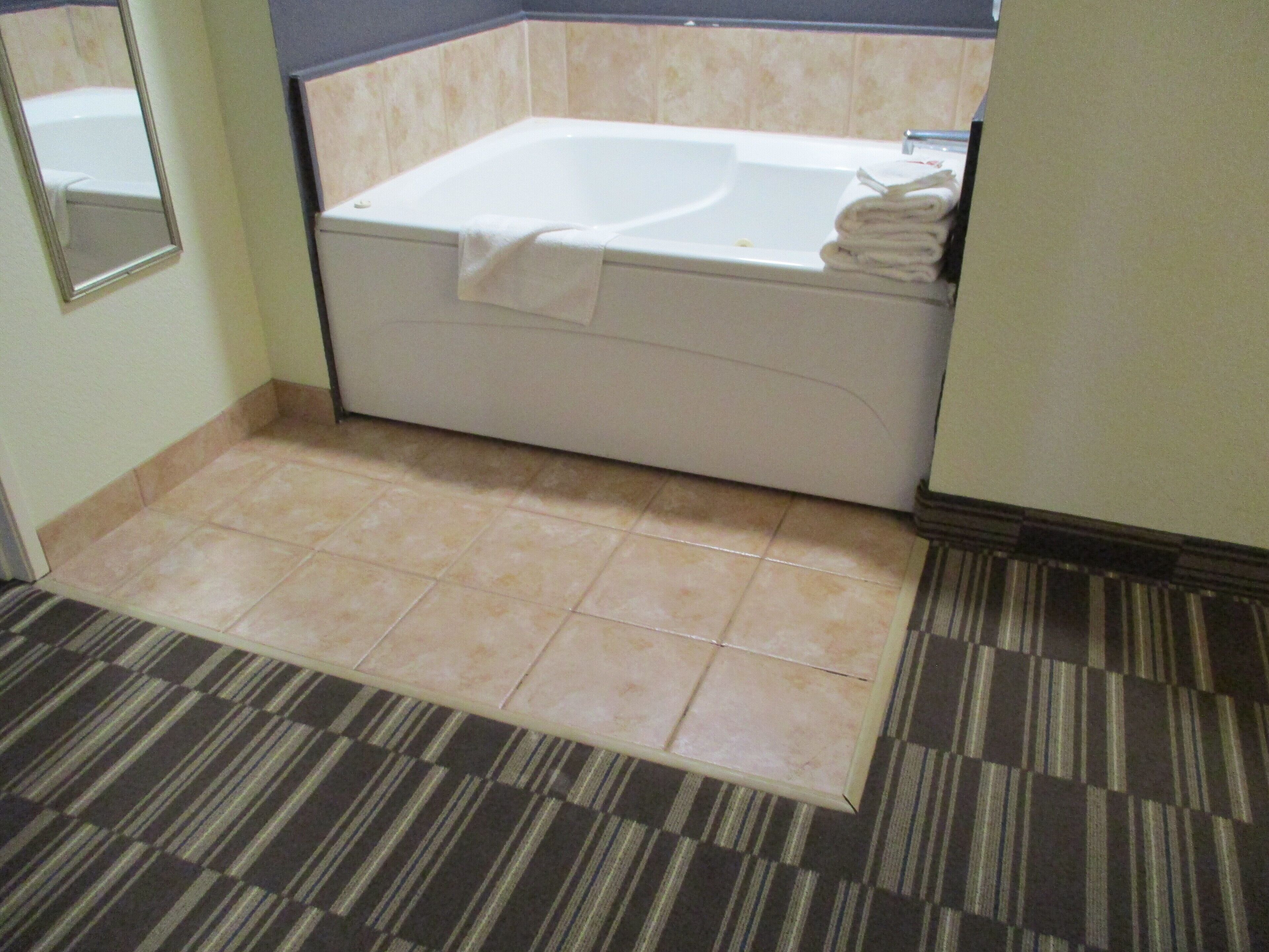 Un baño con bañera, espejo y alfombra a rayas.