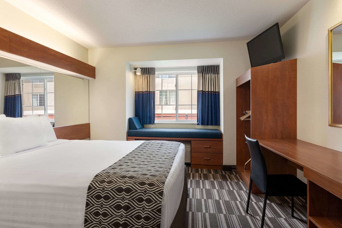 A hotel room with a large bed, a desk, a chair, a television, and a window with curtains.
