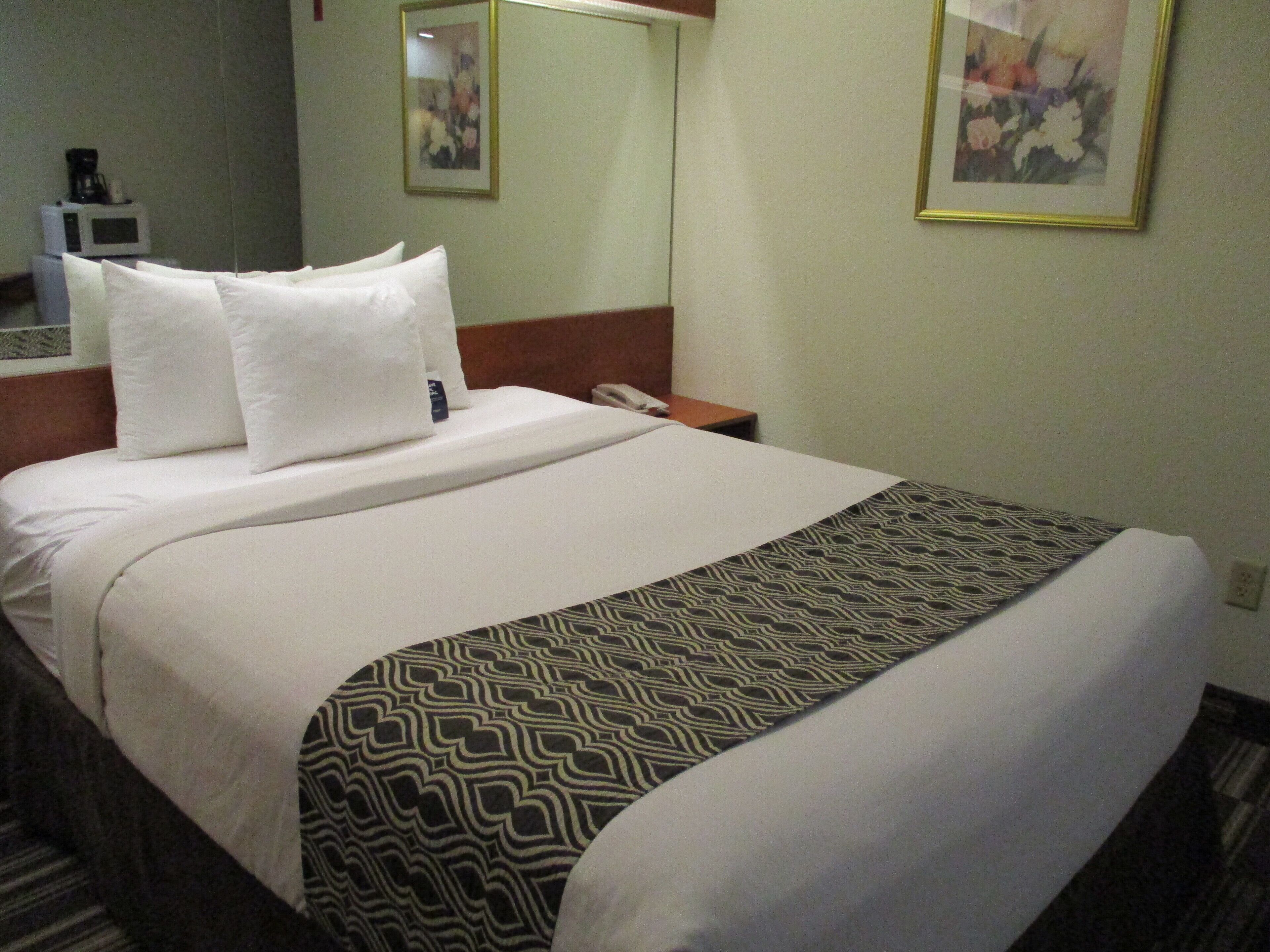 A hotel room with a neatly made bed, a bedside table with a phone, and a microwave in the corner.