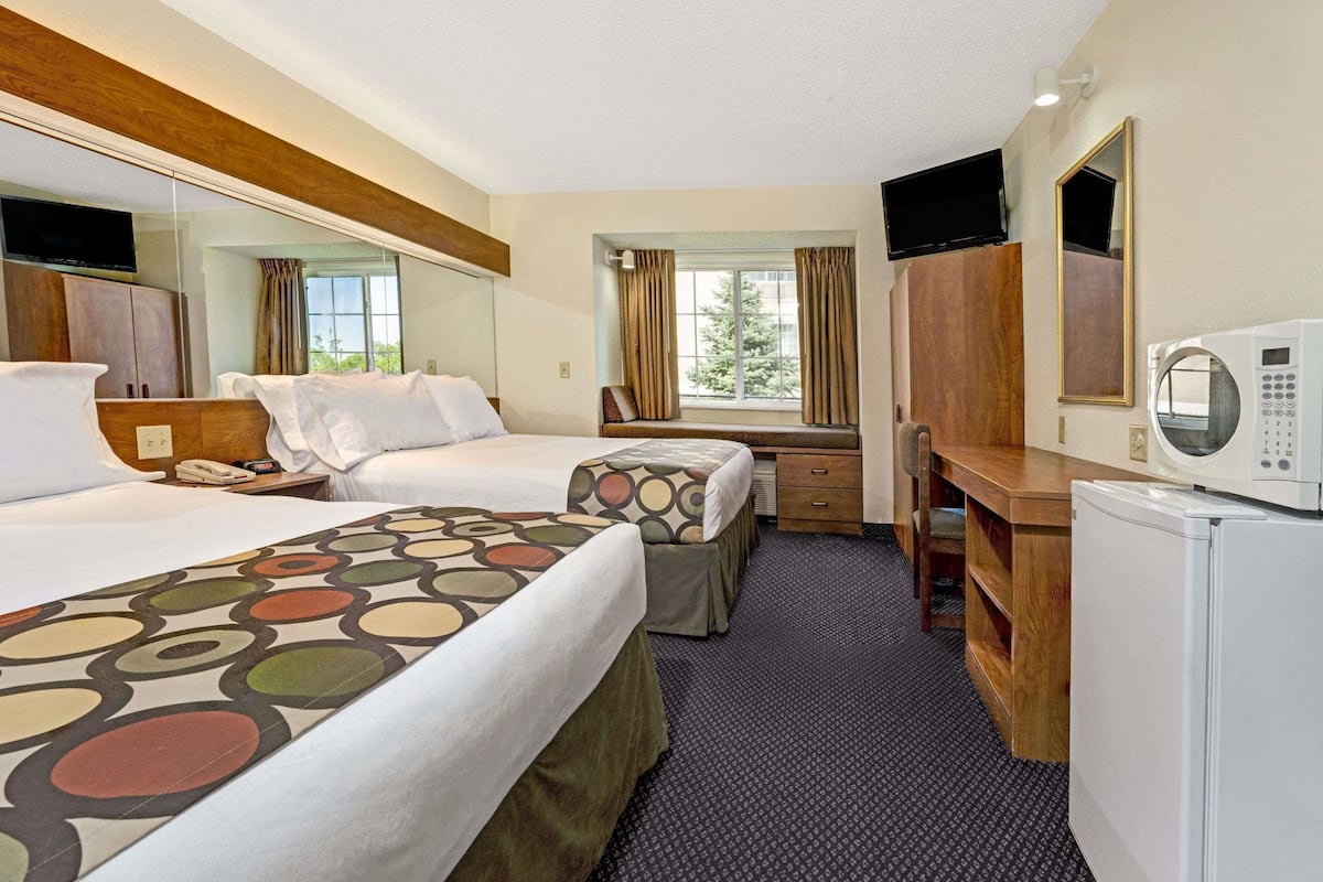 A hotel room with two beds, a desk, a microwave, and a TV.